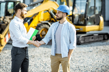 Builder choosing heavy machinery for construction with a sales consultant standing with some...