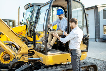 Builder choosing heavy machinery for construction with a sales consultant on the open ground of a shop with special vehicles