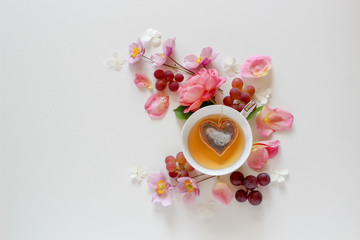Obraz na płótnie Canvas Pink floral arrangement with a cup of tea with a heart shape tea bag inside on a white background