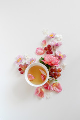 Pink floral composition with a cup of tea and flowers and some grapes on a white background