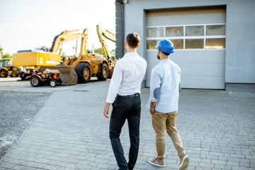 Builder choosing heavy machinery for construction, walking with a sales consultant on the open ground of a shop with special vehicles