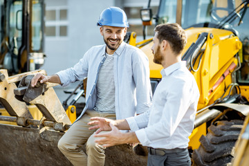 Builder choosing heavy machinery for construction, talking with a sales consultant on the open...