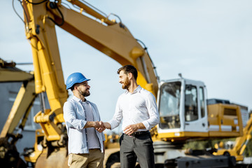Builder choosing heavy machinery for construction, talking with a sales consultant on the open...