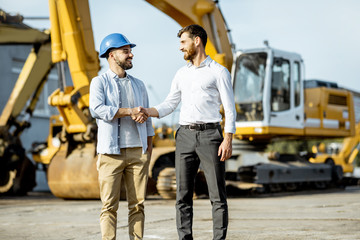 Builder choosing heavy machinery for construction, talking with a sales consultant on the open...