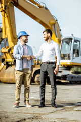 Builder choosing heavy machinery for construction, talking with a sales consultant on the open ground of a shop with special vehicles