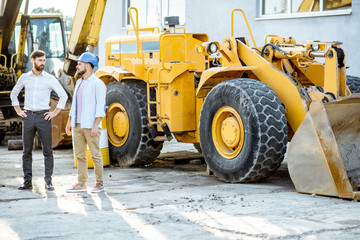 Builder choosing heavy machinery for construction, talking with a sales consultant on the open ground of a shop with special vehicles