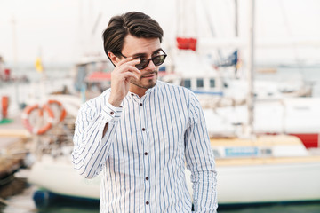 Photo of successful masculine man standing and looking aside while walking on pier