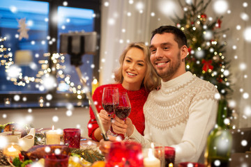 Obraz na płótnie Canvas christmas, holidays, technology and people concept - happy couple in taking picture by selfie stick at home dinner over snow