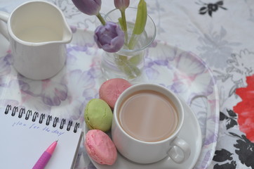 tray with paper sketchbook, smartphone and spring flowers on pink bedding. Relaxing, or working, or writing diary or blog in bed at home.