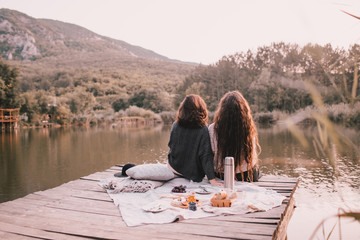 Two women friends having picnic in autumn forest near lake.