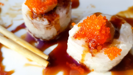 Stylish roll with tempura shrimp in a hot unagi sauce. sushi rolls with chopsticks in sauce on a white plate with food