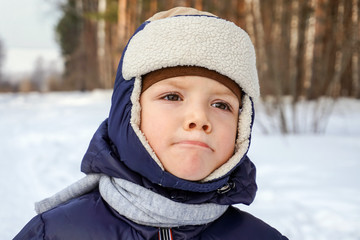 close up portrait of a happy child boy throws snow, snowflakes in the air in cold winter against the background of snowdrifts