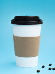Hot white paper cup with coffee beans on blue background. Mockup with copyspace. Coffee shop concept