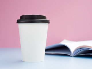 Mockup white paper cup with hot tea or coffee to go with a opened magazine. Side view with Copy Space for text