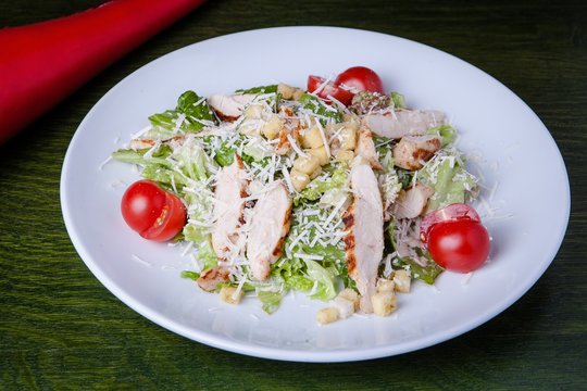 Closeup shot of tasty ceaser salad in a white plate with a green background