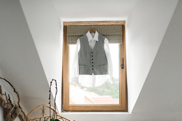 Stylish elegant wedding groom suit hanging on wooden window in hotel room. Groom wedding accessories