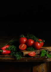 Fresh tomatoes and dill on a dark wooden table on a black background