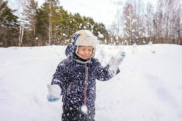 portrait of a happy child boy throws snow, snowflakes in the air in cold winter against the background of snowdrifts