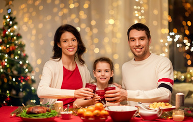 holidays, family and celebration concept - happy mother, father and little daughter having christmas dinner at home