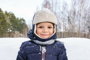 close up portrait of a happy child boy throws snow, snowflakes in the air in cold winter against...