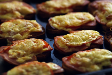 Many baked hot sandwiches with ham and cheese lie on a tray in a row.
