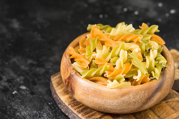 Raw fusilli pasta in a wooden bowl. Dark background
