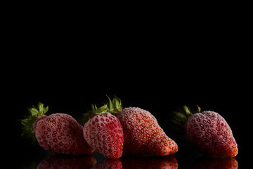 four red frozen strawberries covered with hoarfrost lie on a mirror surface on a black background.