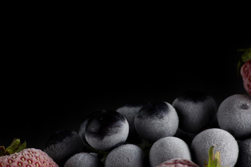 a frozen and frosted bunch of grapes with strawberries lies on the mirror surface of the table on a black background.