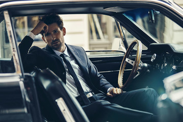 Handsome man in black suit sitting in the old car