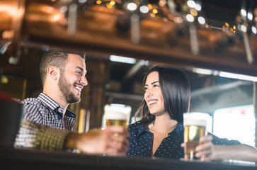 Young couple at beginnings of love story - Pretty woman drinking beer with handsome man at pub -...
