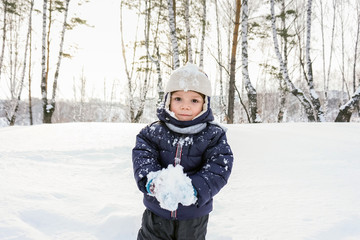 Fototapeta na wymiar portrait of a happy child boy throws snow, snowflakes in the air in cold winter against the background of snowdrifts