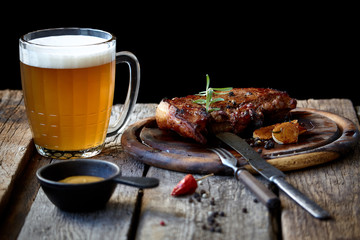 Still life with a big fried steak, a glass of beer, mustard and cutlery on an old wooden tabletop, the concept of Oktoberfest and St. Patrick's Day