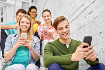 education, technology and learning concept - group of happy international high school students or classmates with smartphones sitting on stairs