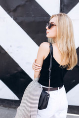 Obraz premium Lifestyle urban fashion trendy portrait of young cute blondie girl dressed in black and white clothes walking in the city in summer day