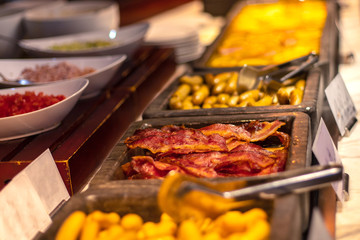 Buffet breakfast at a Chinese hotel. Closeup bacon on blurry background of food trays. Breakfast is included in the hotel.