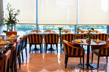 Served tables in the hotel restaurant. The banquet room is ready to receive guests. Roller blinds omitted and a Chinese plant in the corner.