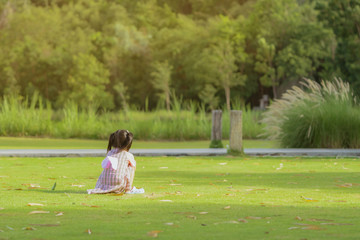 A little girl in a pink skirt enjoys a relaxing time playing on the green lawn at the public park in the evening.