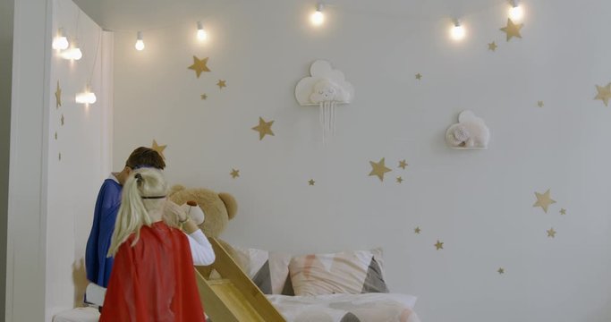 120 FPS SLOW MOTION Cute funny little Caucasian kids boy and girl wearing capes and masks playing in the bedroom, pretending to be superheroes. 4K UHD