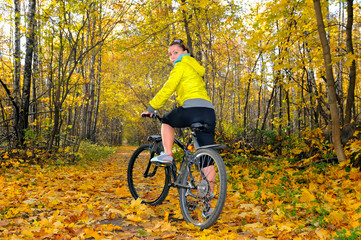Fototapeta na wymiar Girl with a bicycle on an alley in autumn forest