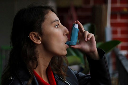 Health and medicine - Young girl using blue asthma inhaler to prevent an asthma attack.