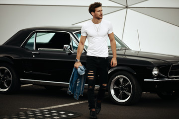 Fototapeta na wymiar Handsome man with black old car waliking on the parking