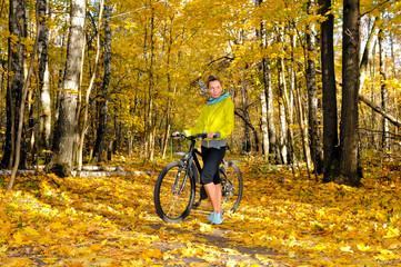 Fototapeta na wymiar Girl with a bicycle on an alley in autumn forest