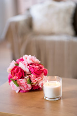 decoration, hygge and cosiness concept - burning fragrance candle and flower bunch at cozy home