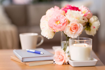 decoration, hygge and cosiness concept - burning fragrance candle, flower bunch, books and pen on wooden table