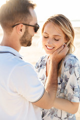 Photo of caucasian romantic couple smiling and hugging while walking on sunny beach
