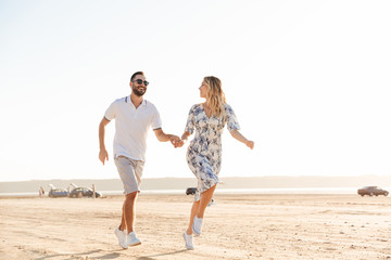 Photo of caucasian happy couple smiling and running on sunny beach