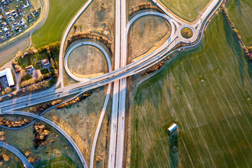Fototapeta na wymiar Aerial top view of modern highway road intersection, house roofs on spring green field background. Drone photography.