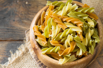 Colored fusilli pasta in a wooden bowl on a wooden table. Rustic style