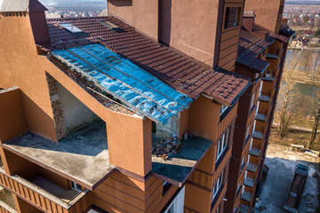 Aerial top view of unfinished tall apartment building, annex room under construction, high chimneys and plastic windows on tiled roof.