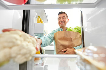 eating, diet and storage concept - smiling middle-aged man with new purchased food in paper bag...